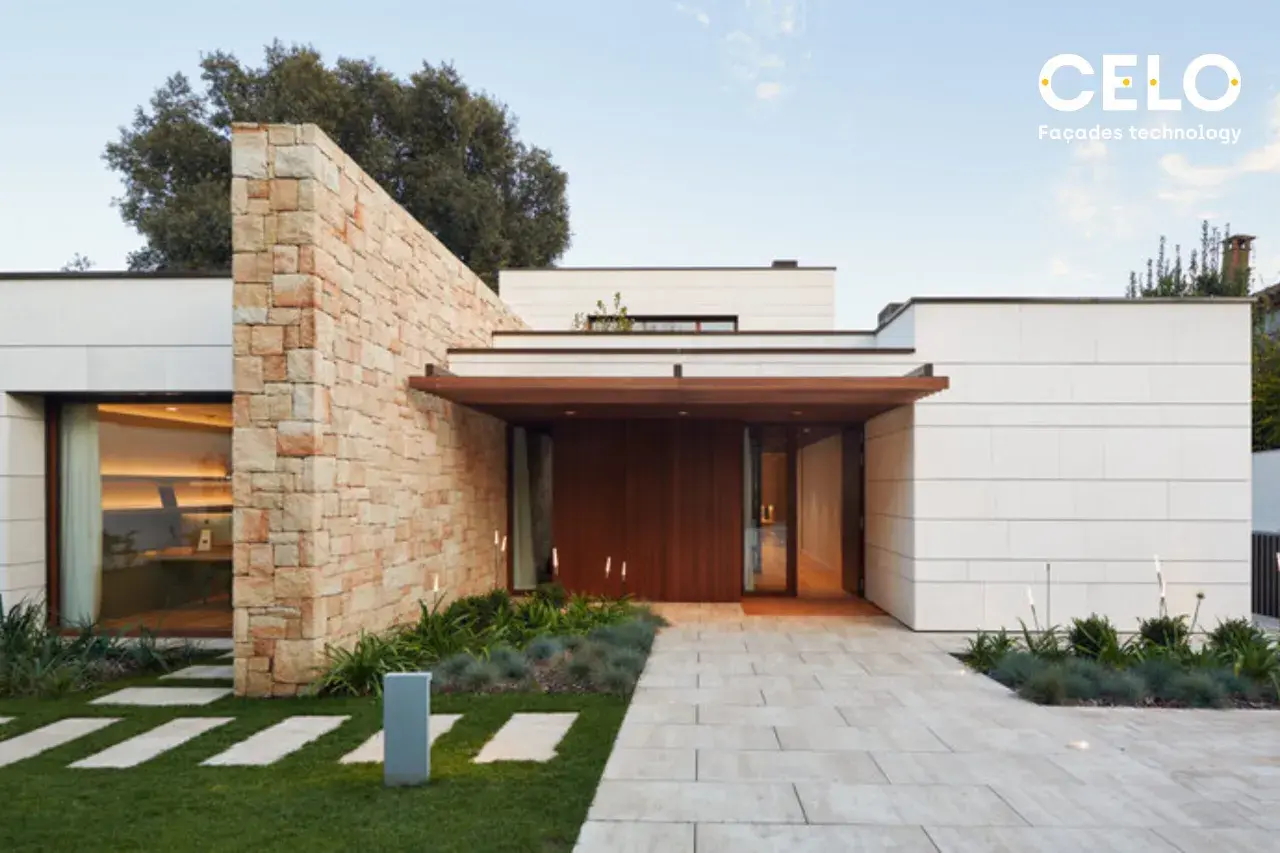 Casa moderna con acabados de fachadas de piedra y paneles blancos. Un camino de baldosas conduce a la entrada principal de madera.
