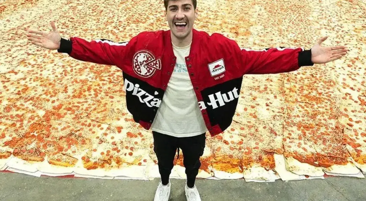 Mężczyzna w kurtce Pizza Hut stoi na gigantycznej pizzy.