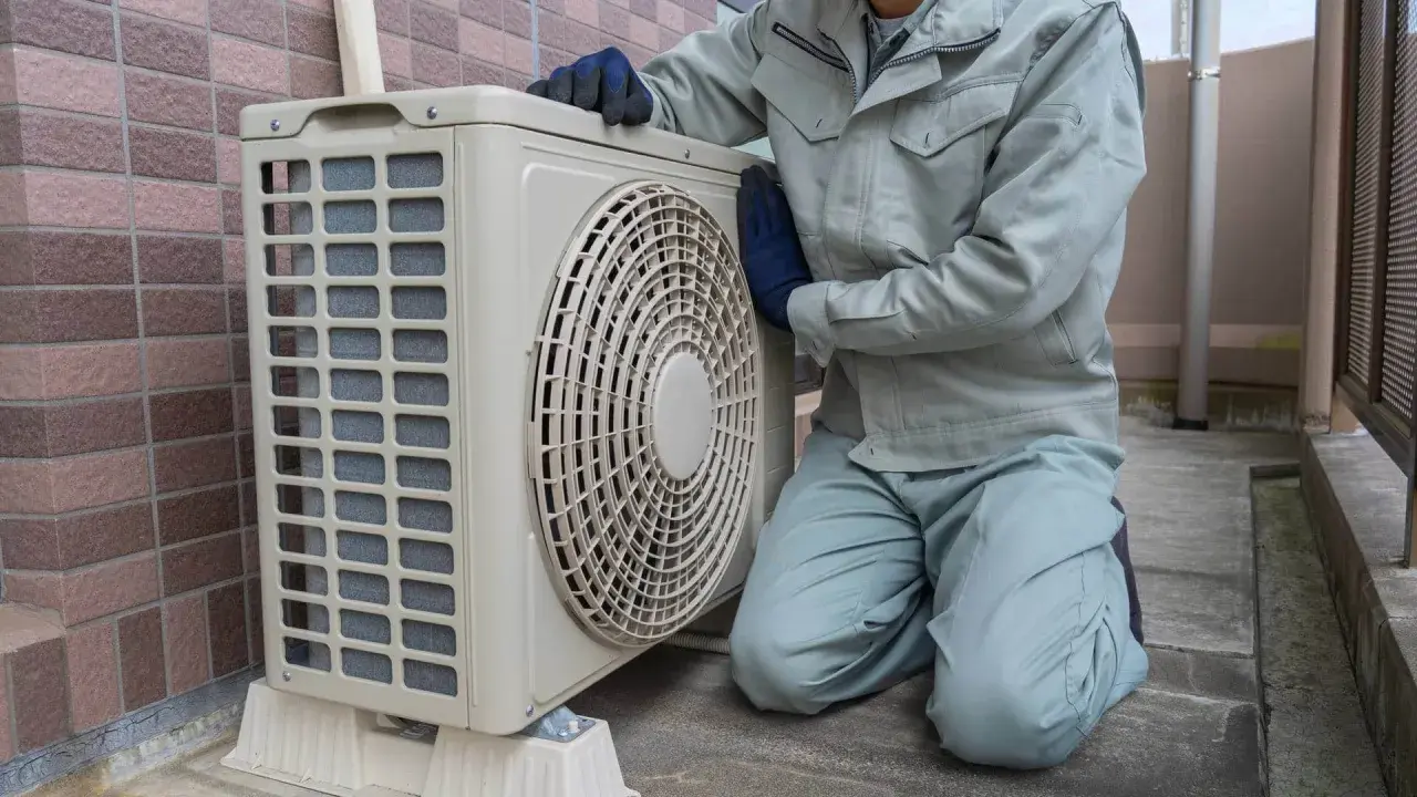 Pracownik w rękawiczkach sprawdza jednostkę zewnętrzną klimatyzacji. Wzór pozwolenia na montaż klimatyzacji w bloku jest kluczowy dla takich prac.
