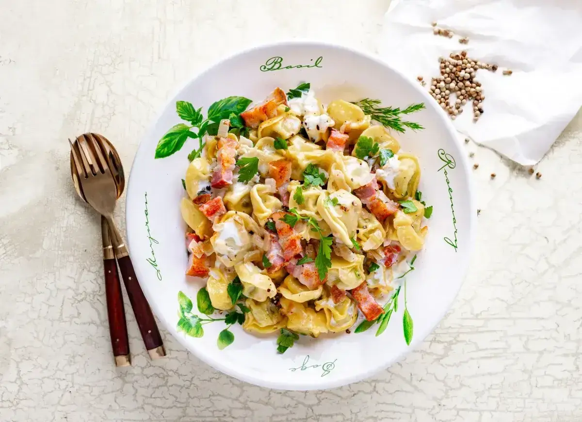 Pyszne tortellini z boczkiem i śmietanowym sosem, idealne jako pomysł na obiad. Posypane natką pietruszki.