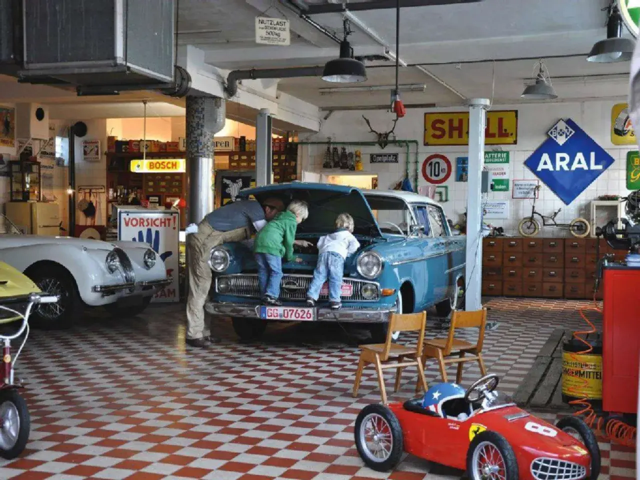 Familie inspiziert blauen Oldtimer in Werkstatt. Die Restaurierung des Autos scheint ein gemeinsames Projekt zu sein.