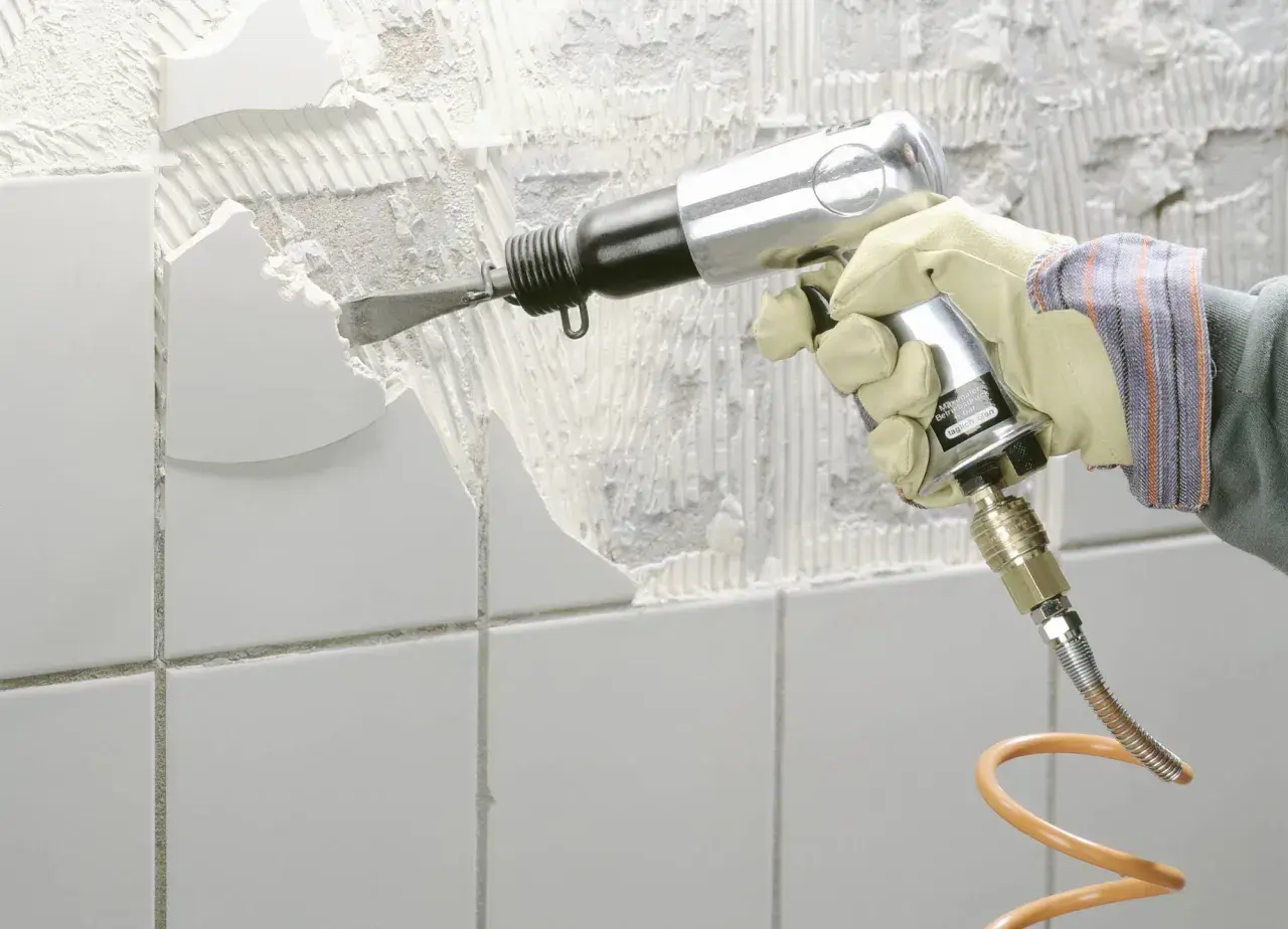 Mit einem Pressluftmeißel wird alter Fliesenkleber von der Wand entfernt.