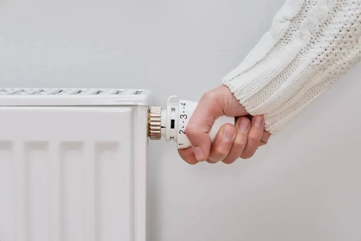 Mano ajustando el termostato de un radiador. El radiador solo calienta un lado, indicando un posible problema de circulación.