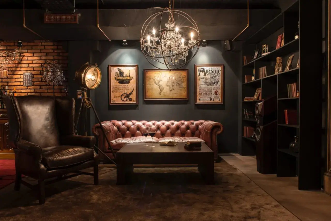 Sofá de cuero, sillón y mapa del mundo en una sala con decoración steampunk. Lámpara de pie industrial y estanterías llenas de libros.