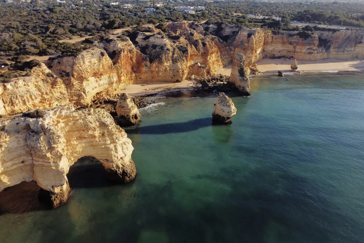 Skaliste klify Algarve, z łukiem skalnym i samotnymi formacjami, wpadają do turkusowego morza. Widok przypomina o urokach wybrzeża, jakbyśmy byli w pobliżu Faro Lizbona.