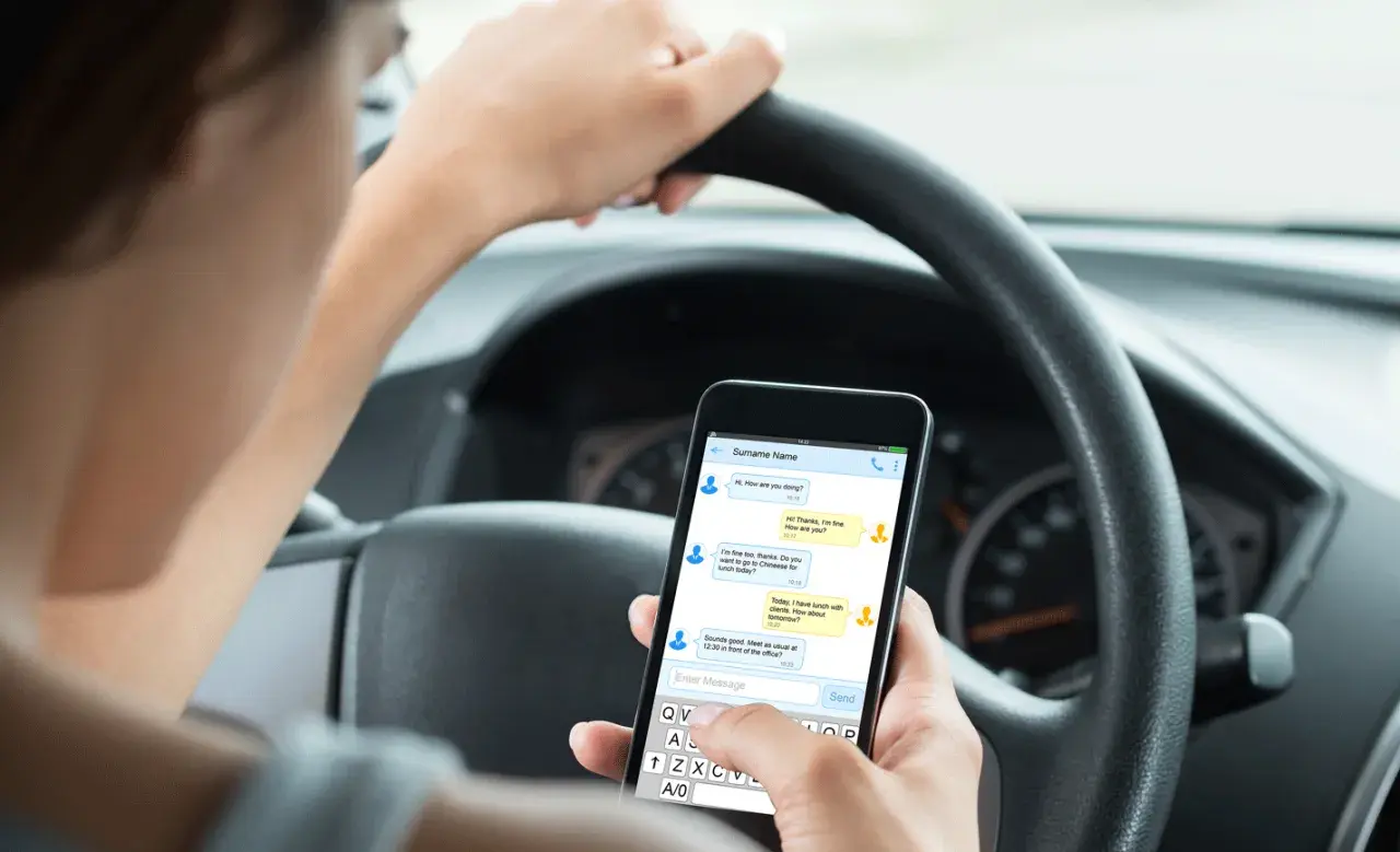 Person håller en telefon i bilen och skriver ett meddelande.