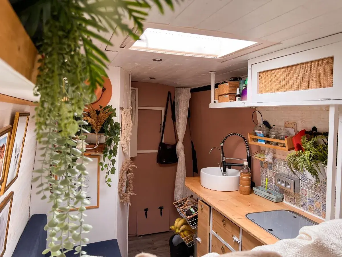 Intérieur de fourgon aménagé : cuisine avec évier, robinet, placards et plantes.