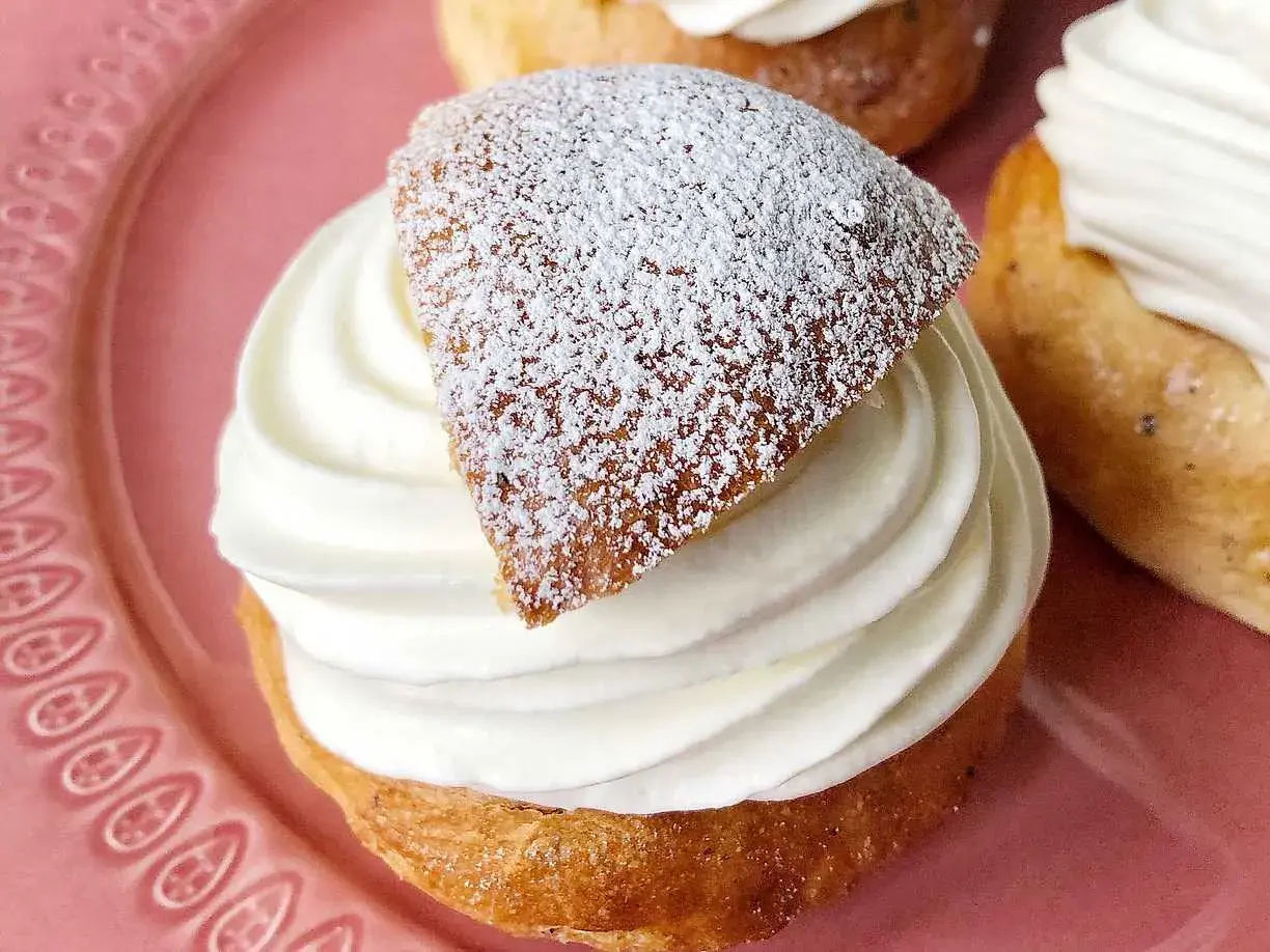 En gammaldags semla med fluffig grädde och pudrat lock på en rosa tallrik.