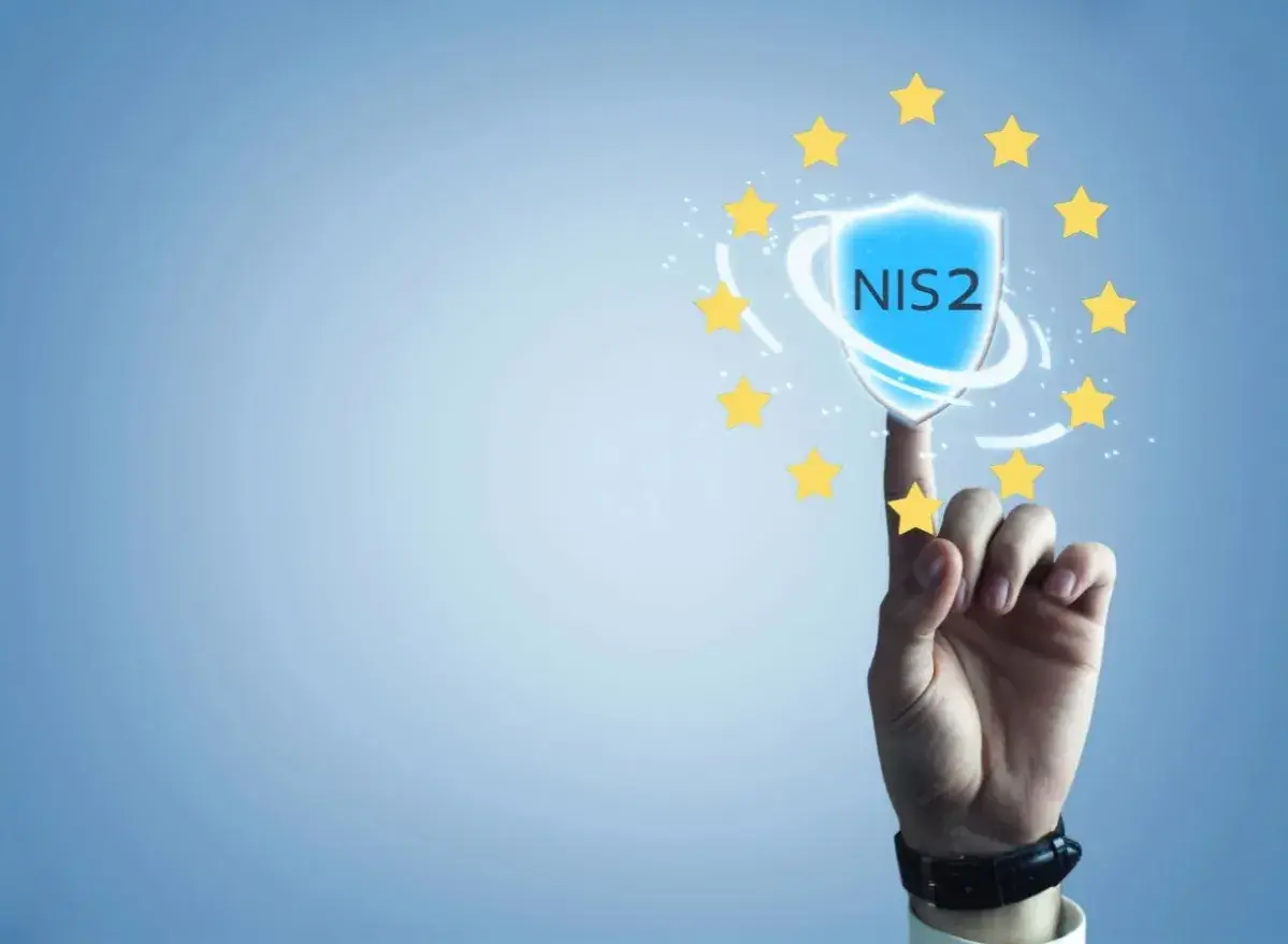 Palec wskazujący dotyka tarczy z napisem NIS2, otoczonej gwiazdkami Unii Europejskiej. Symbolizuje to bezpieczeństwo i zgodność z dyrektywą NIS2.
