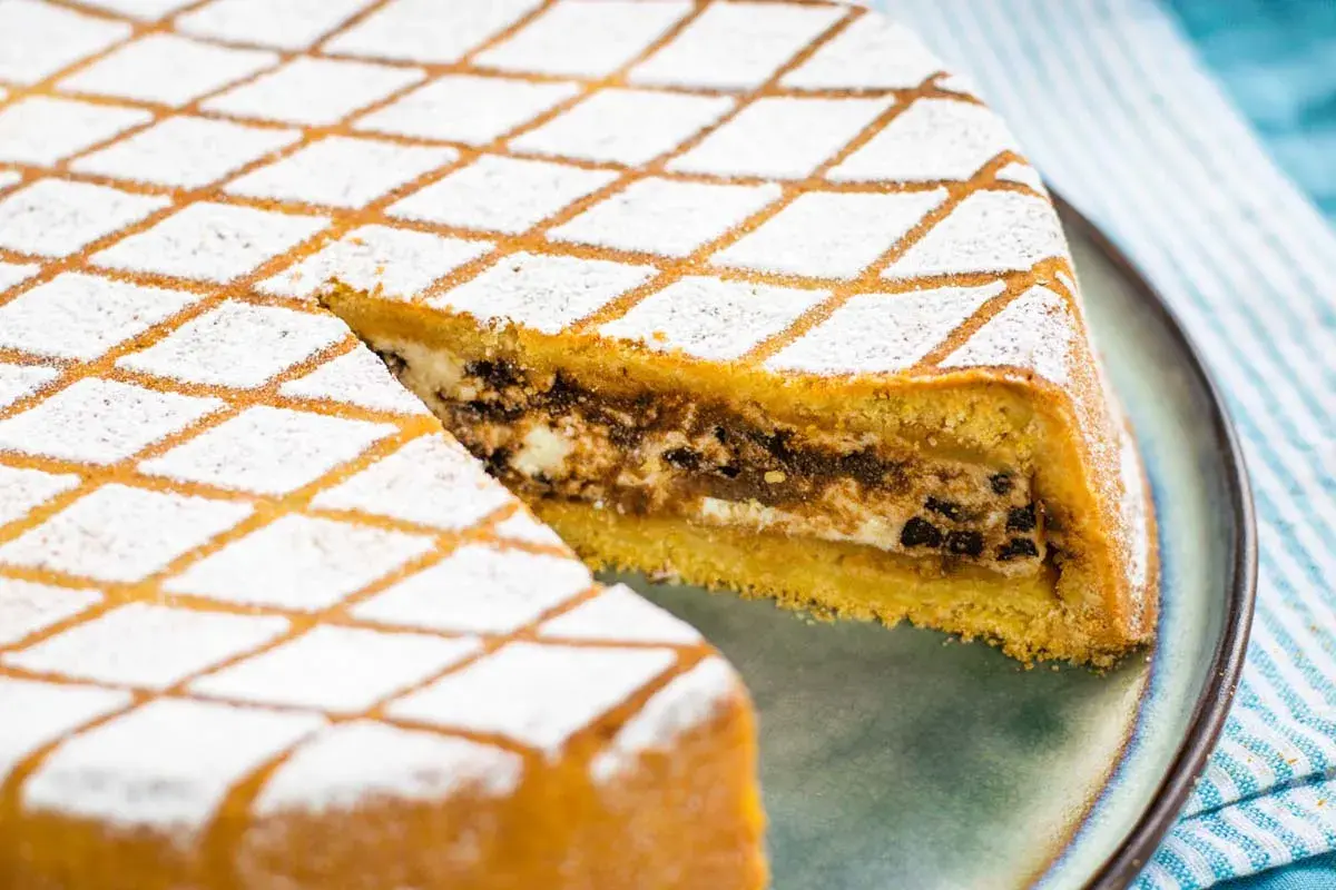 Una fetta di cassata al forno, con la sua copertura a rombi di zucchero a velo, rivela un ripieno goloso di ricotta e cioccolato.