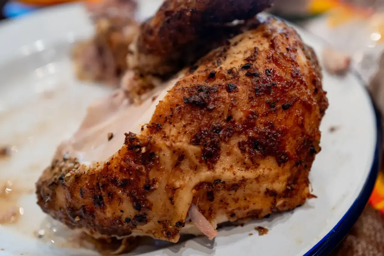 Un morceau de poulet au four cuisson lente, doré et savoureux, servi sur une assiette blanche.
