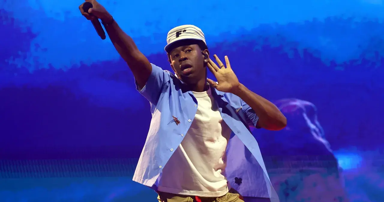 Tyler The Creator w Krakowie, w niebieskiej koszuli i czapce, z mikrofonem w dłoni.