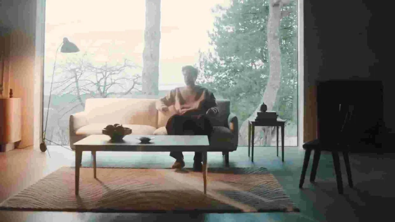 En person sitter i en soffa i ett rum med dansk design inredning. Ett stort fönster visar en vinterskog.