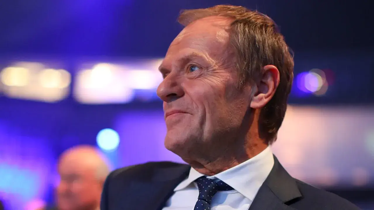 Uśmiechnięty mężczyzna w garniturze, z lekko przerzedzonymi włosami. Czy Tusk jest rudy? Jego włosy mają odcień jasnego brązu.