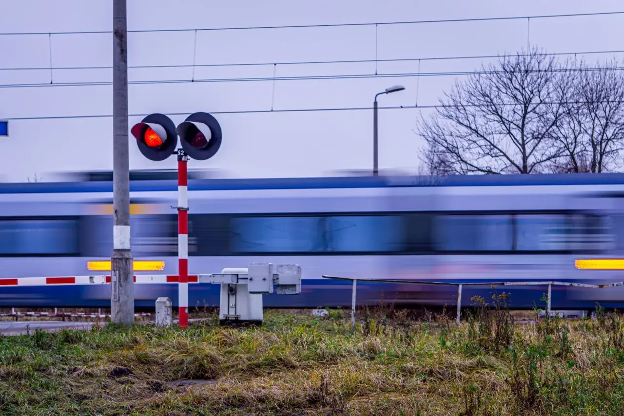Pędzący pociąg mija przejazd kolejowy z czerwonymi światłami, zgodnie z nowym rozporządzeniem o przejazdach kolejowych.