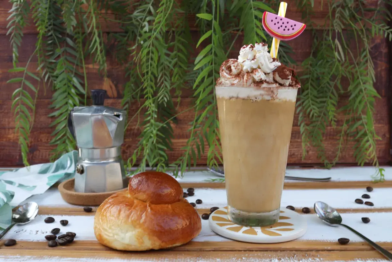 Un bicchiere di caffè freddo siciliano con panna e cacao, accanto a una brioche e una moka.