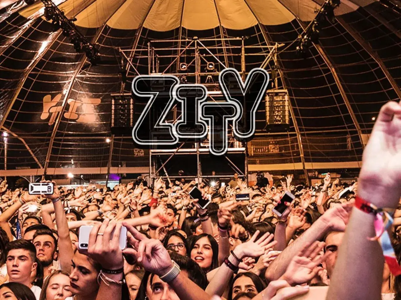 Multitud animada en la entrada del espacio Zity, con brazos en alto y móviles grabando el evento.
