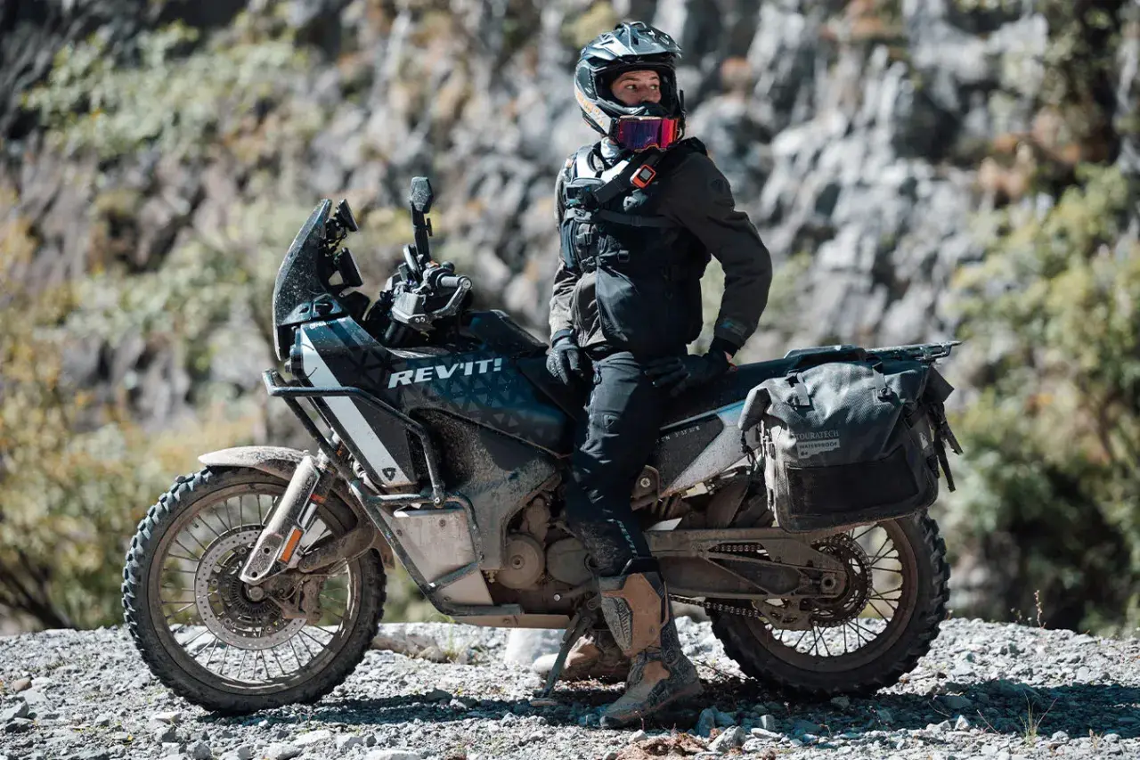 Motociclista con equipo **waterproof** listo para la aventura. ¿Será **Gore-Tex**? La moto, su compañera en terrenos difíciles.