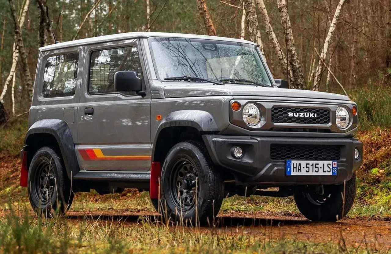 Szary Suzuki Jimny 2026 z kolorowymi pasami na boku, gotowy na terenową przygodę w lesie.