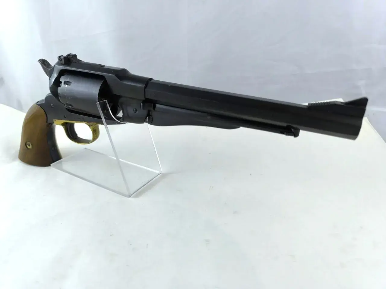 Czarny rewolwer Uberti Remington 1858 z drewnianą rękojeścią, prezentowany na przezroczystym stojaku.