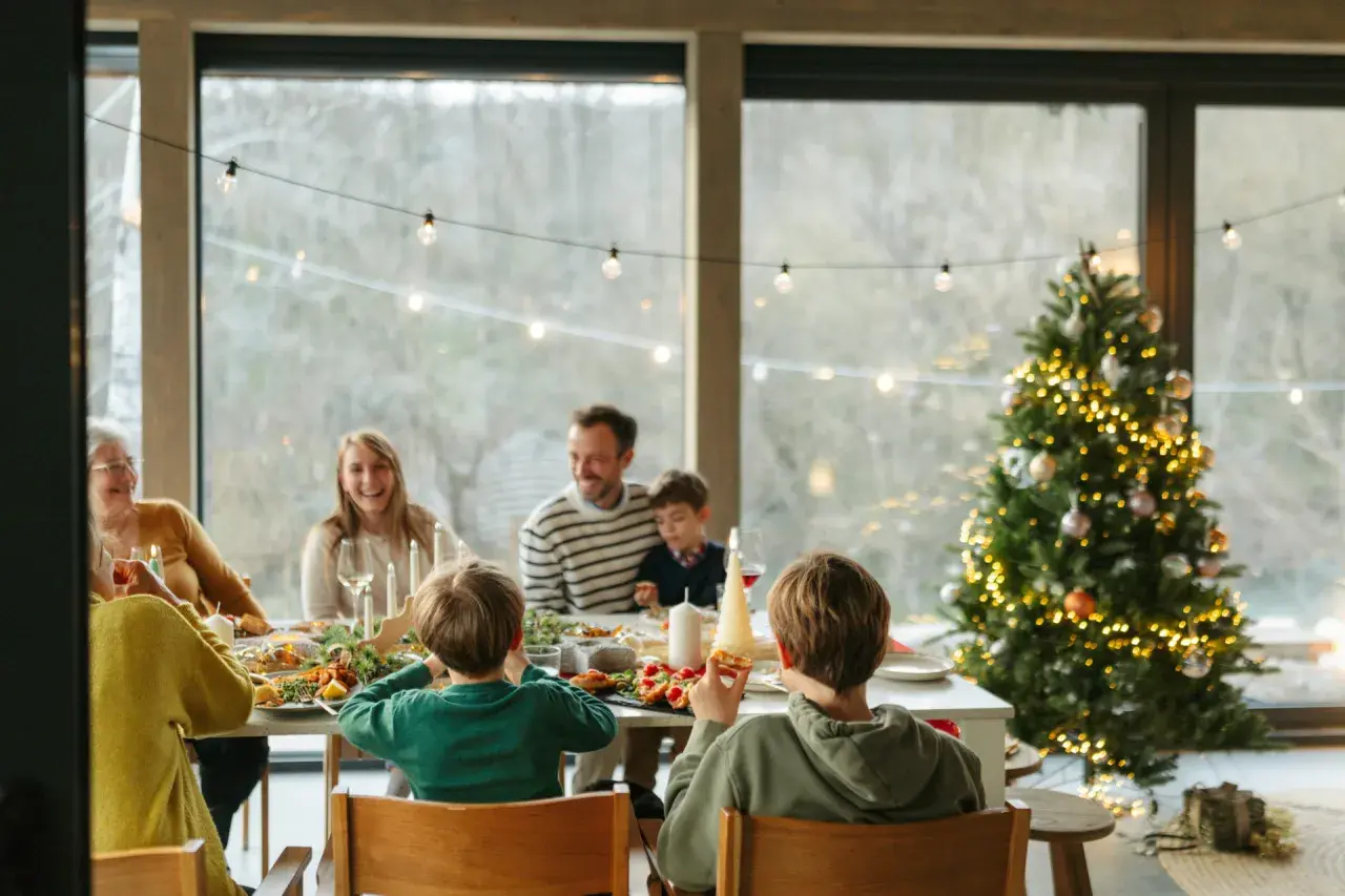 Familie feiert Weihnachten am festlich gedeckten Tisch, mit geschmücktem Baum im Hintergrund.