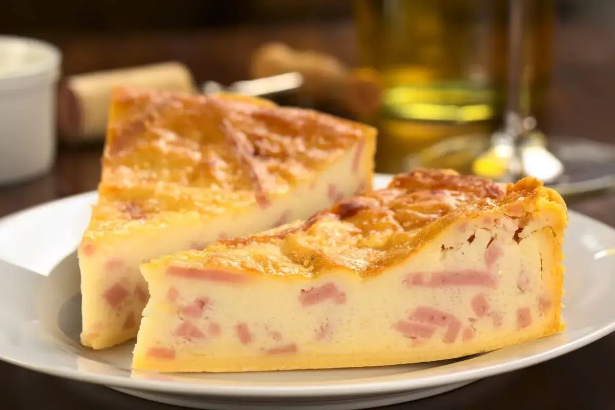 Deux parts de quiche jambon fromage dorée sur une assiette blanche, avec un verre de vin en arrière-plan.