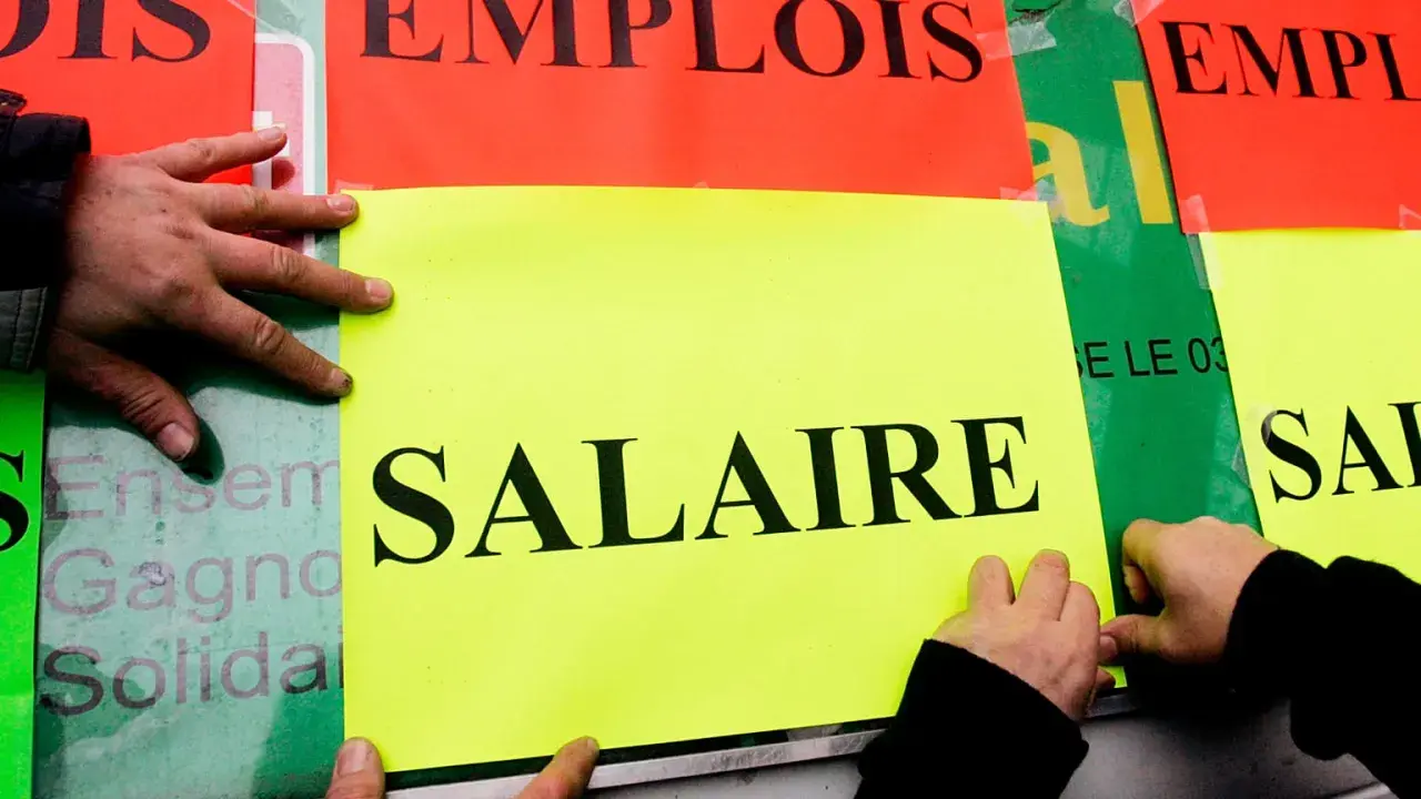 Ręce przyklejają plakaty z napisem "SALAIRE" (płaca). Ludzie walczą o najlepsze zarobki w Europie.