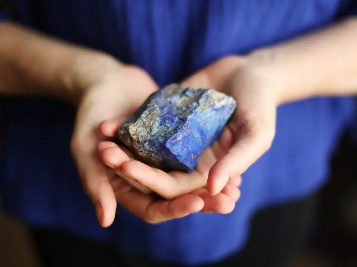 Manos sostienen un trozo de lapislázuli, su intenso azul resalta contra la tela azul.