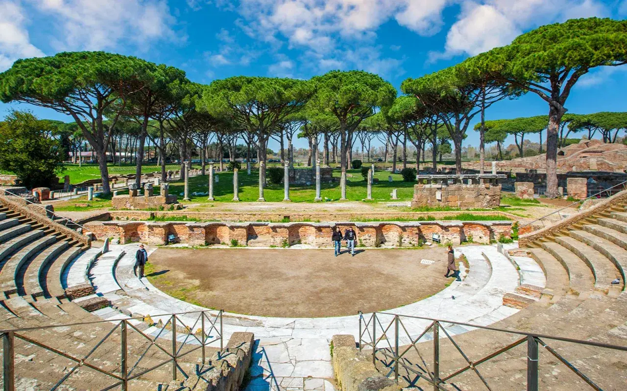Antico teatro romano a Ostia Antica, Roma, con pini marittimi che incorniciano le rovine.