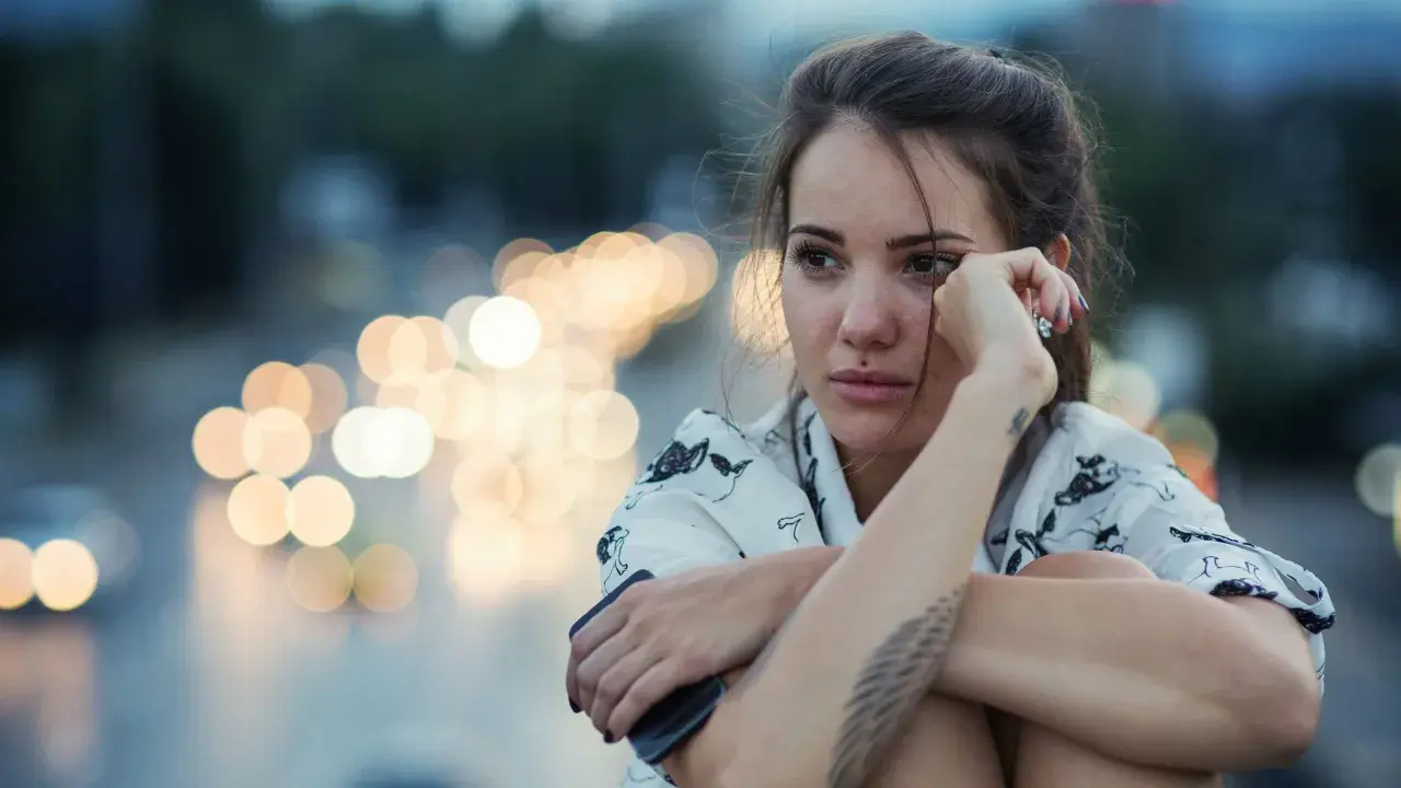 Giovane donna pensierosa, con luci sfocate sullo sfondo, sembra voler rimuovere ricordi traumatici.