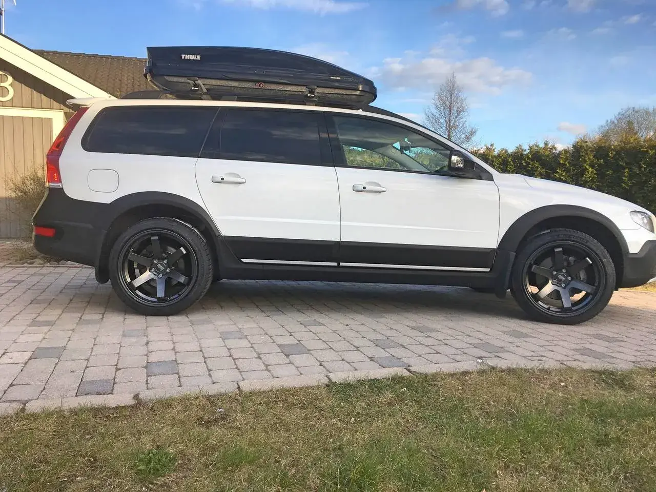 Vit Volvo XC70 2016 med takbox och svarta fälgar. Kanske ett problem med att få plats med allt bagage?