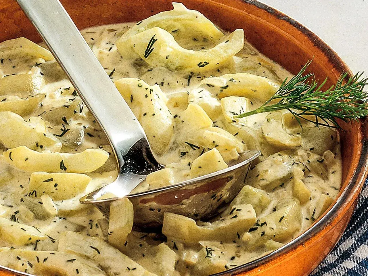 Cremige geschmorte Gurken mit Dill in einer Terrine, serviert mit einer Schöpfkelle.