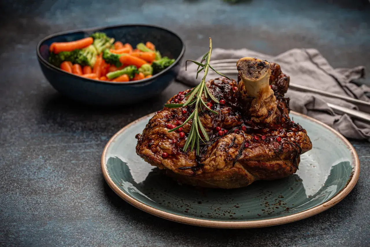 Un savoureux jaret de porc rôti, glacé et parsemé de baies roses, servi avec des légumes vapeur.