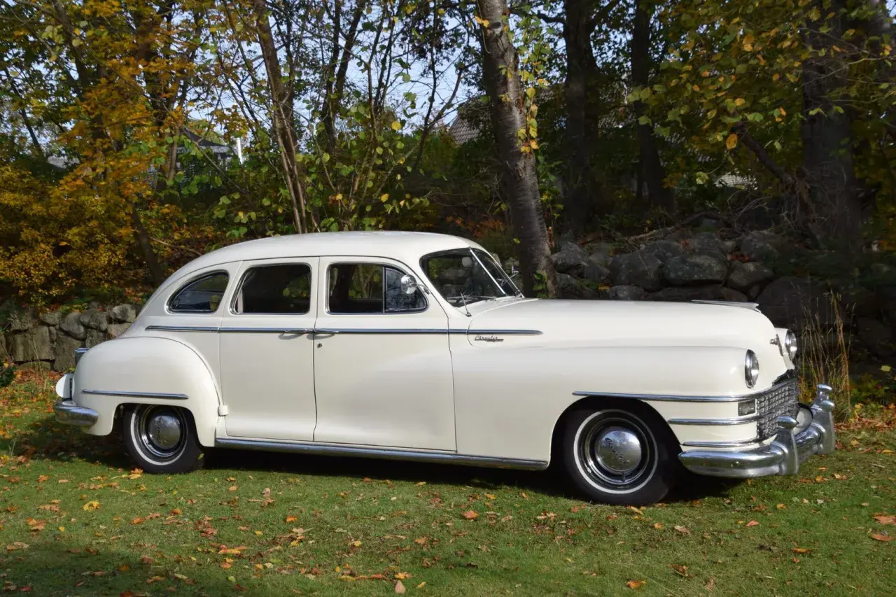 En vit Chrysler New Yorker från 1940-talet står parkerad på en gräsmatta med höstlöv.