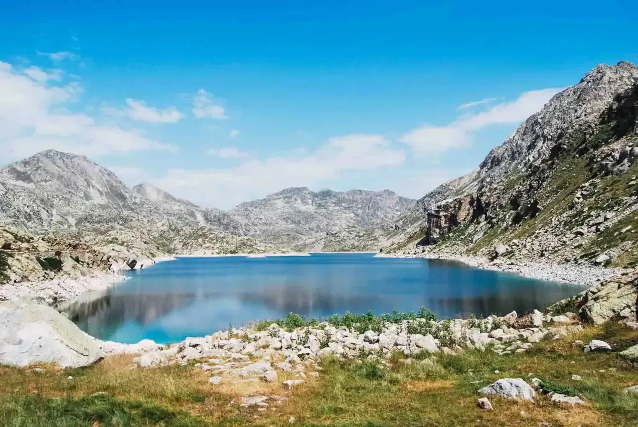 Un lago azul profundo en la vall fosca que ver, rodeado de montañas rocosas y cielo azul con nubes.