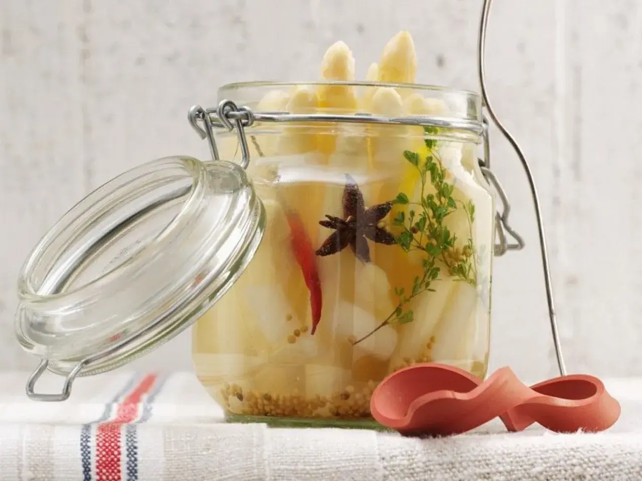 Ein Glas mit eingelegtem Spargel, Gewürzen und Kräutern. Der Deckel ist geöffnet.