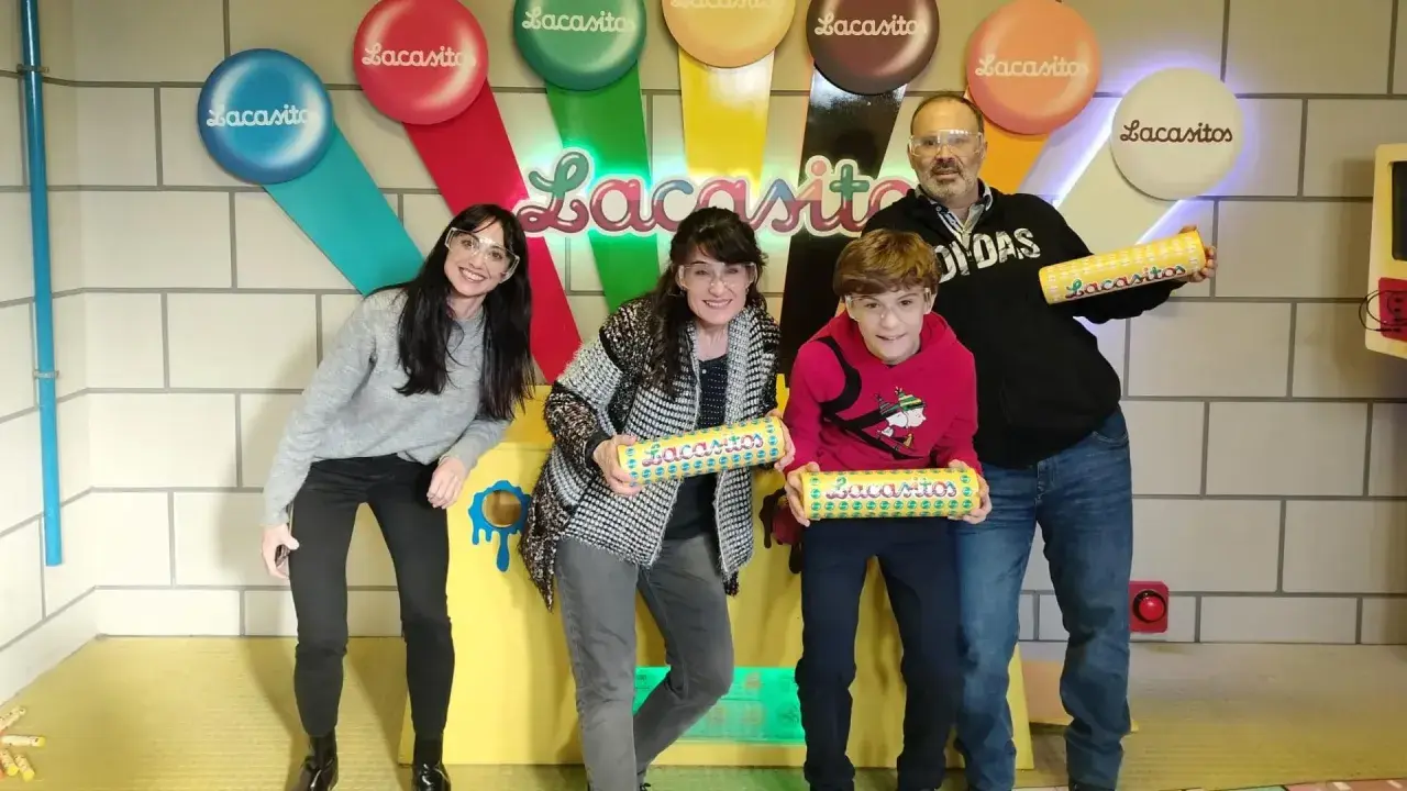 Familia sonriente posa con tubos de Lacasitos en un escape room temático. ¡Una aventura dulce y divertida!