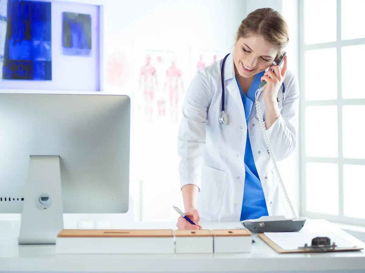 Medico al telefono, impegnato nella gestione appuntamenti, mentre scrive su un blocco note.