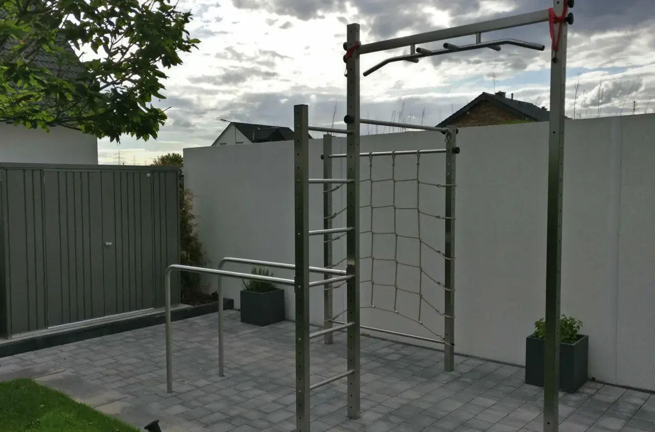 Eine Klimmzugstange für draußen mit Kletternetz und Barren im Garten. Perfekt für ein Outdoor-Workout.