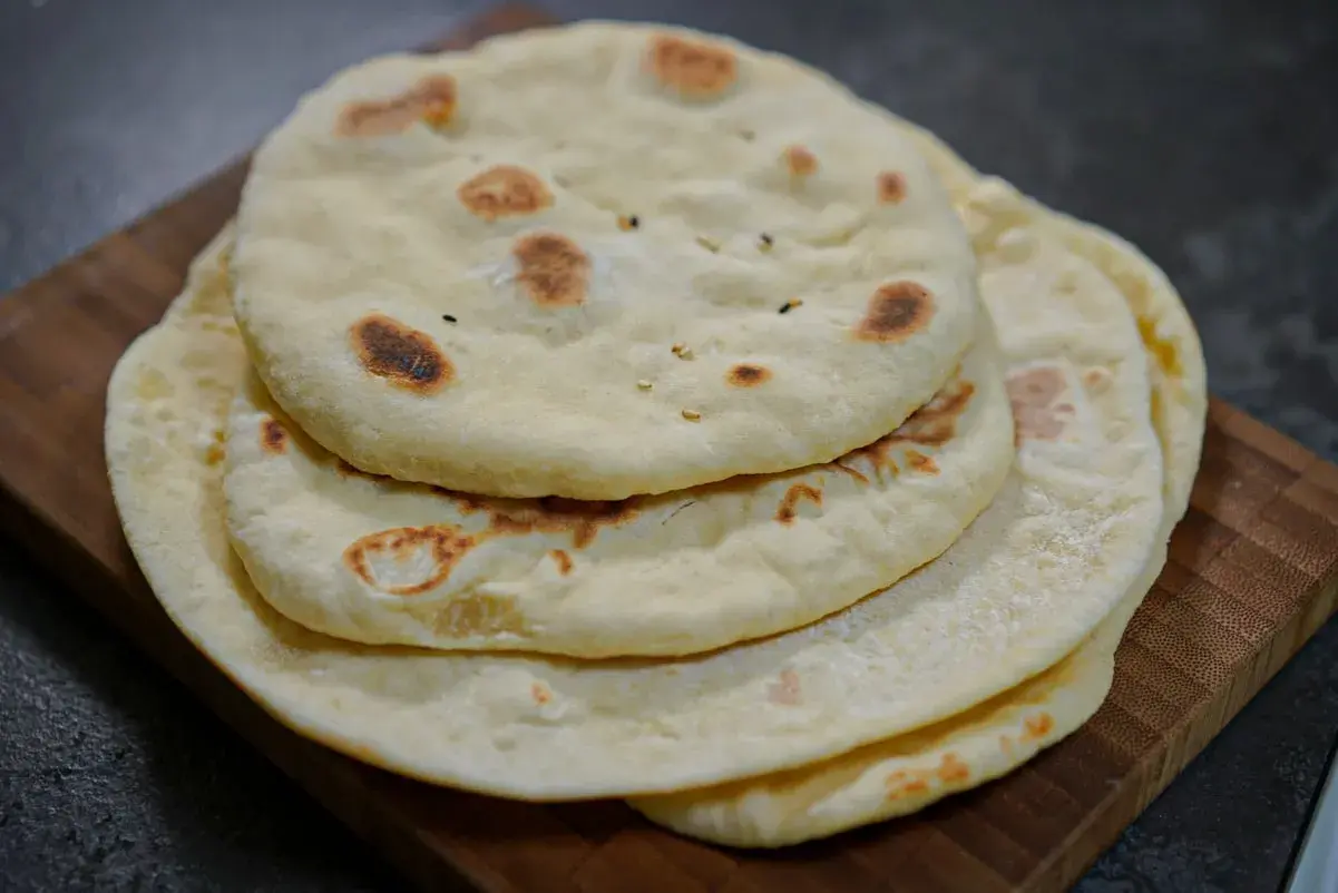 Pile de pains arabes moelleux, légèrement dorés par la cuisson, sur une planche en bois. Parfait pour accompagner un repas.