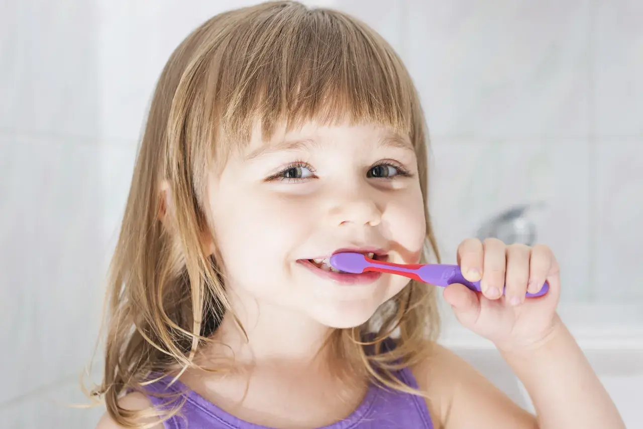 Bambina sorridente si lava i denti con un dentifricio al fluoruro di sodio per un sorriso smagliante.