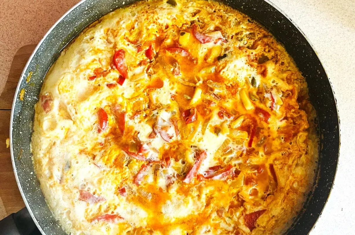 Pyszny omlet z warzywami w trakcie smażenia na patelni. Widoczne kawałki papryki i cebuli.