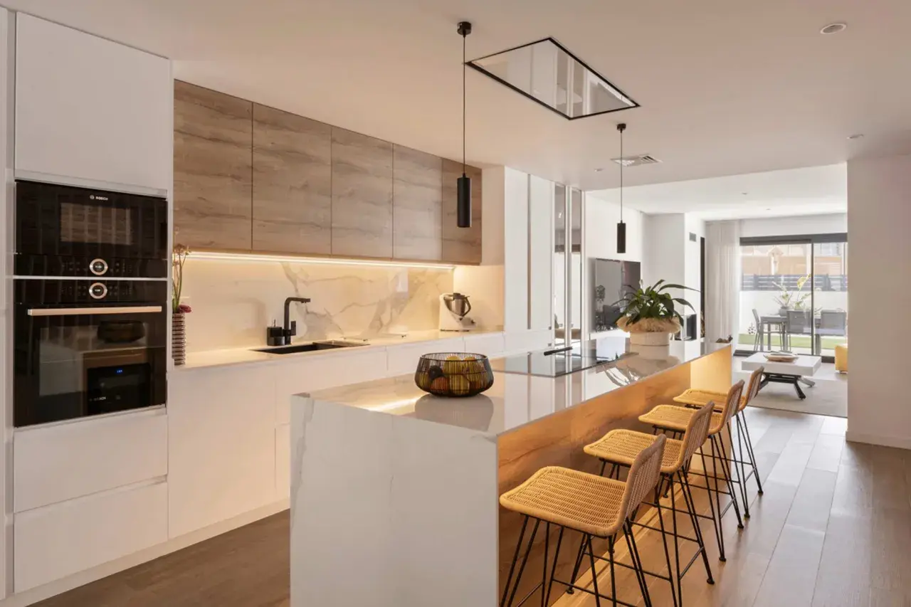 Cocina moderna con isla, encimera de mármol y lámpara barra led iluminando el espacio.