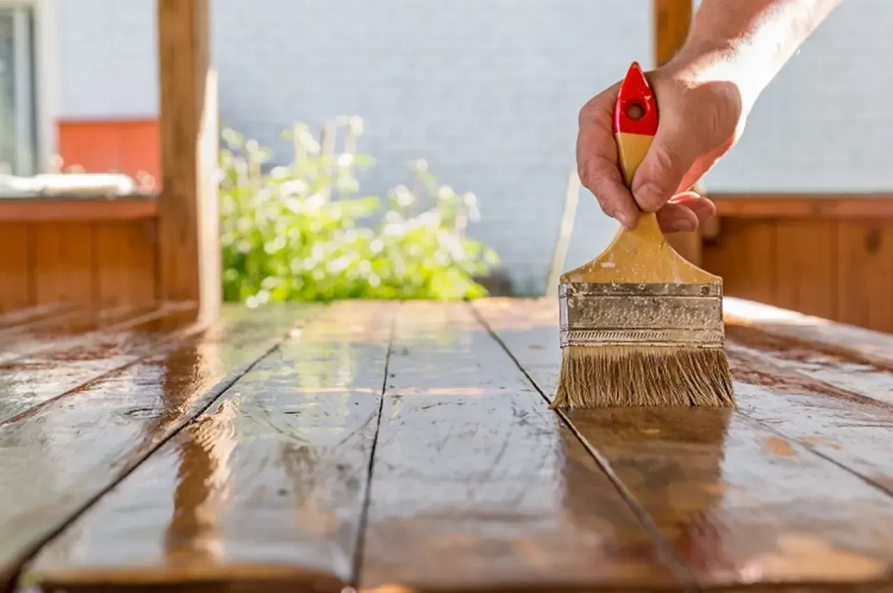 Mano aplicando barniz a una mesa de madera. El proceso de lijar después de barnizar es clave para un acabado perfecto.