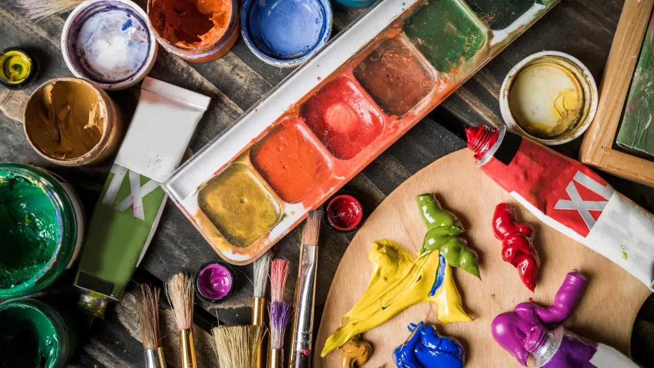 Palette d'un artiste peintre acrylique avec tubes de peinture, pinceaux et godets de couleurs vives sur fond de bois.
