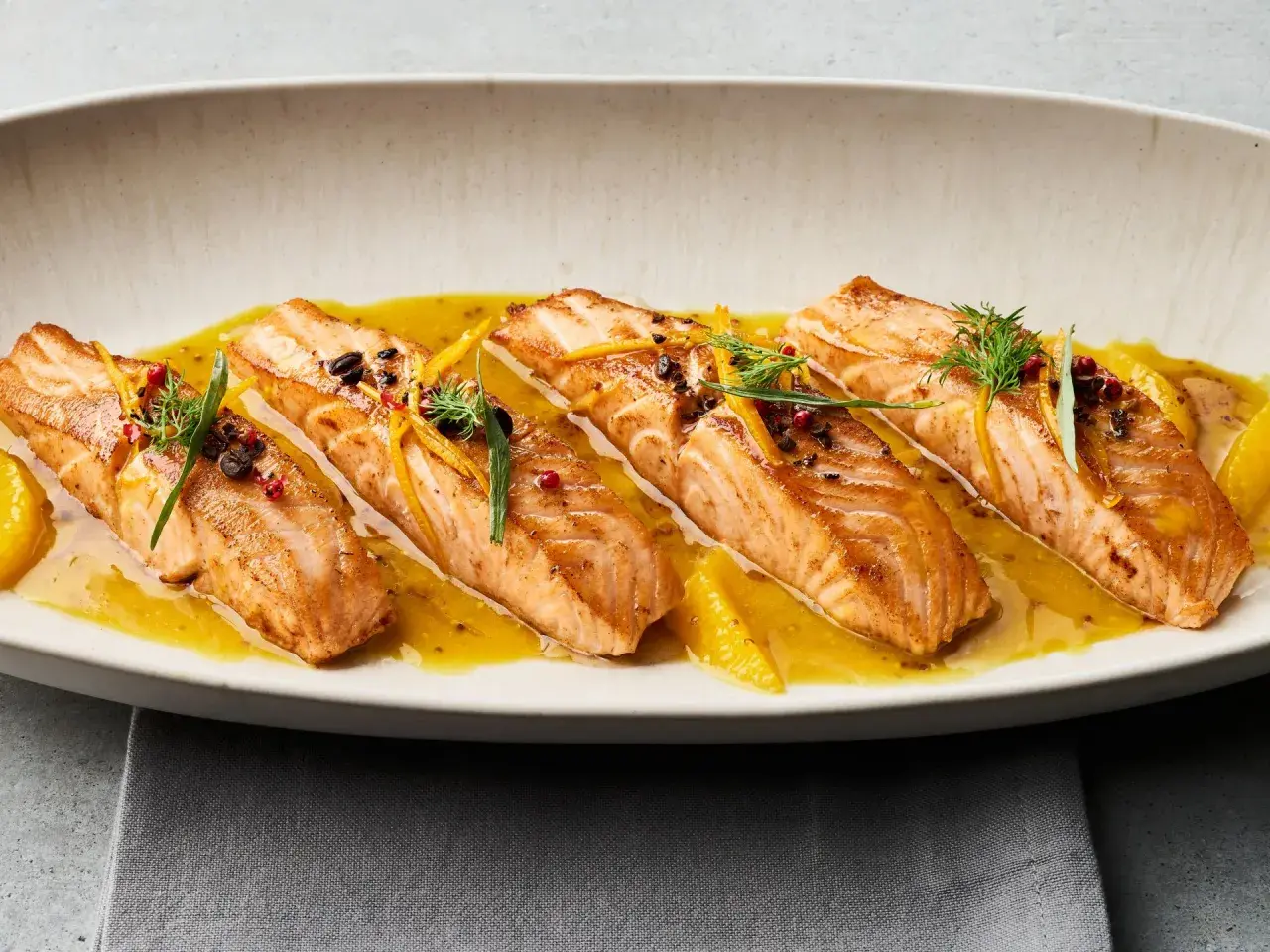 Gebratene Lachsfilets auf einer Zitrussoße, garniert mit Dill und Orangenzesten. Tolle Ideen für eine Fischplatte!