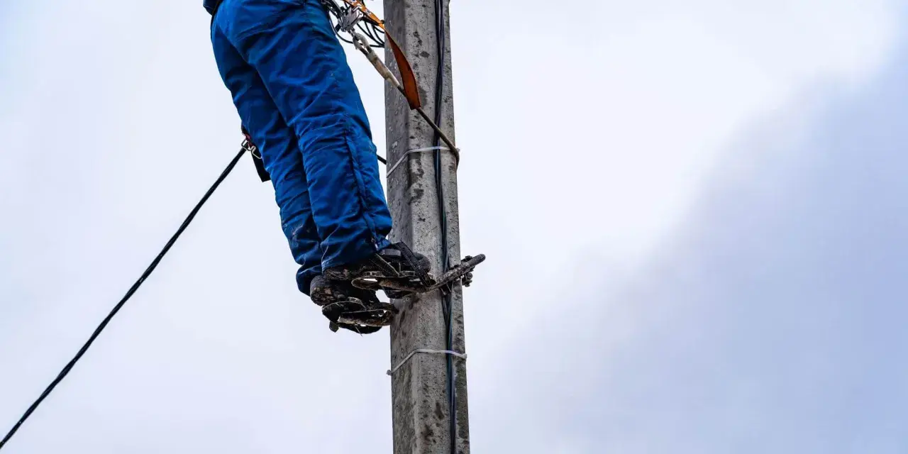 Energetyka chce zakopać kabel na mojej działce. Pracownik na słupie w niebieskich spodniach i z przyrządami.