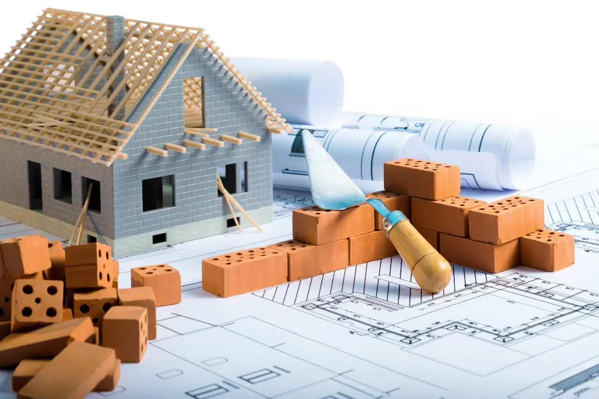 Modello di casa in costruzione su progetti, mattoni e cazzuola. Pianificazione per il rinforzo fondazioni esistenti.