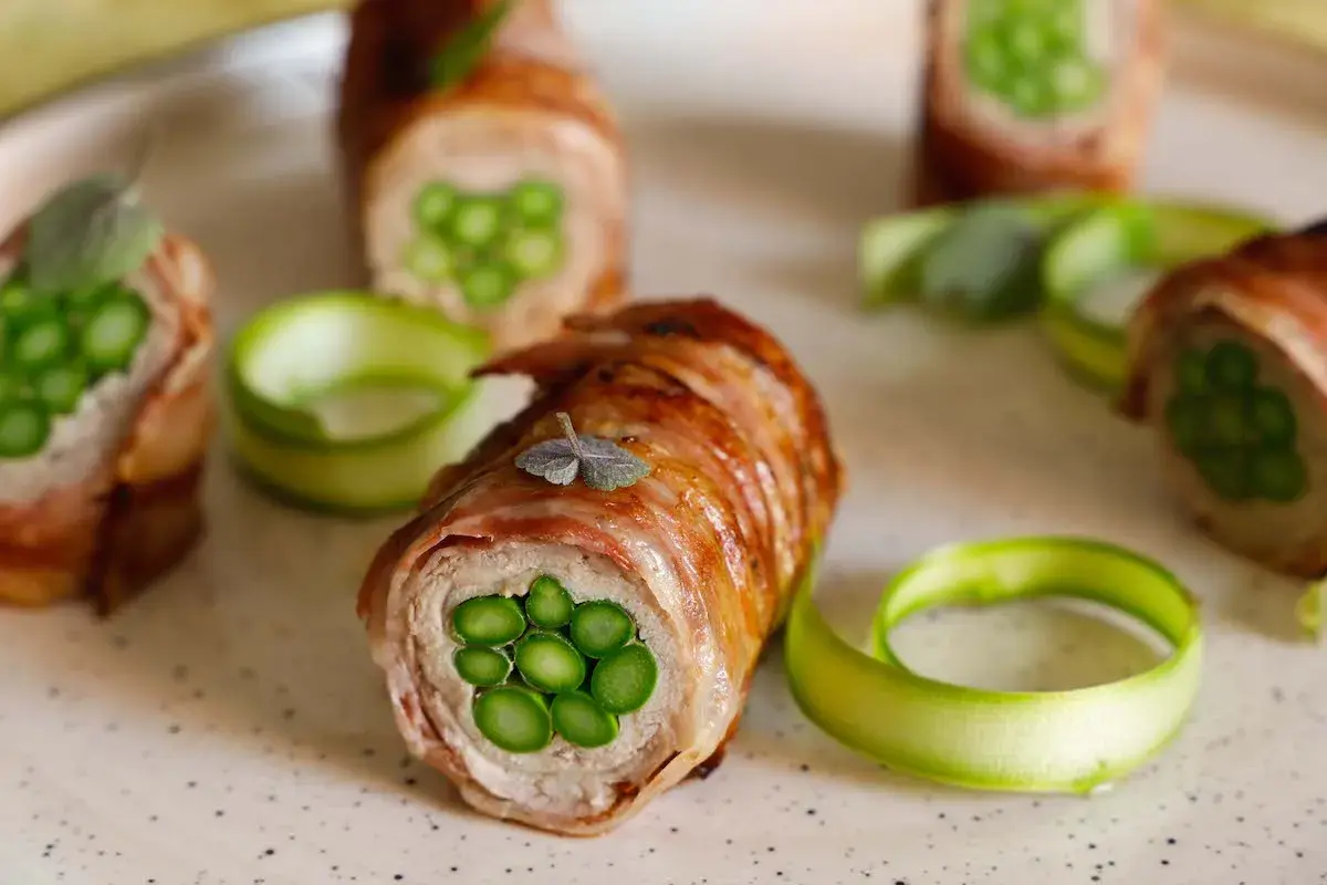 Deliziosi involtini di carne con asparagi freschi, avvolti in pancetta croccante e guarniti con erbe aromatiche.