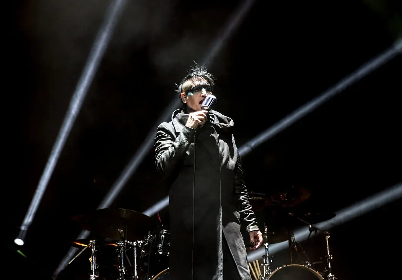 Marilyn Manson na scenie w Warszawie, w czarnym płaszczu i z charakterystycznym makijażem, śpiewa do mikrofonu.